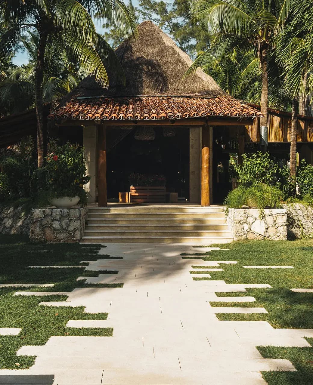 Stone pathway through gardens leading to a palapa-roofed building