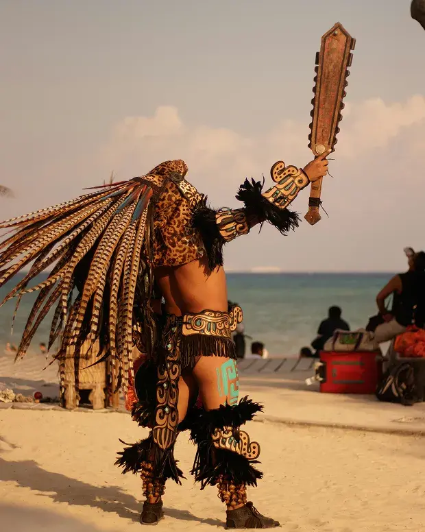 Danzante maya con vestimenta tradicional de plumas frente al mar