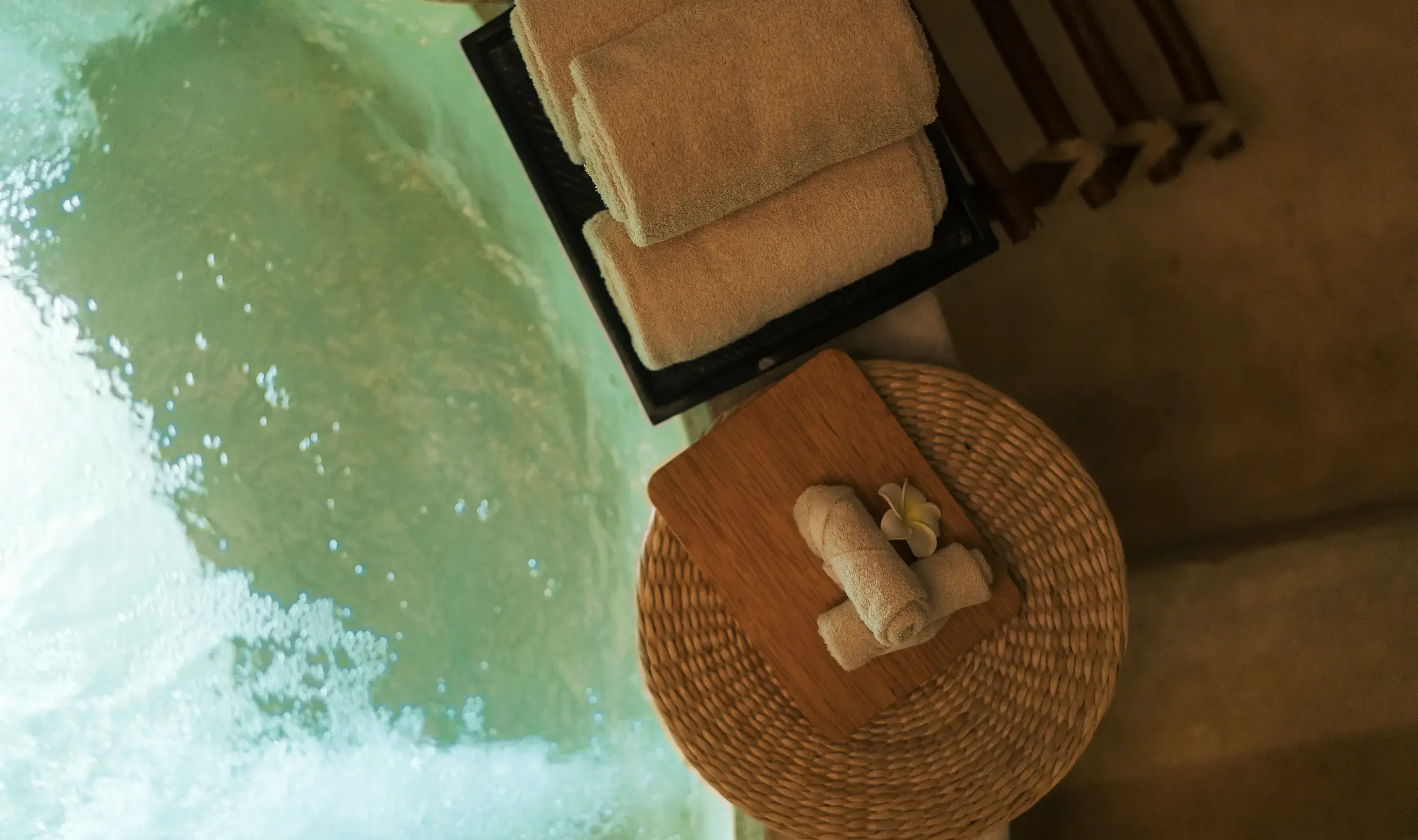 Rolled spa towels and a frangipani flower next to the bathtub