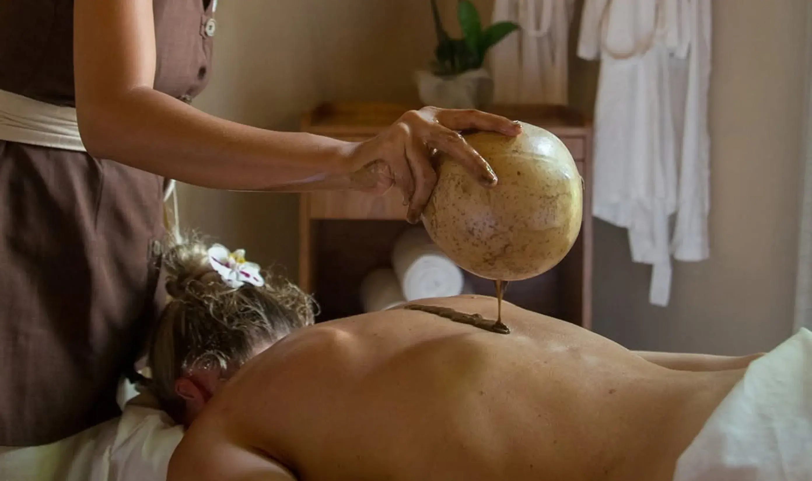 Therapist applying a warm herbal compress massage on a guest's back