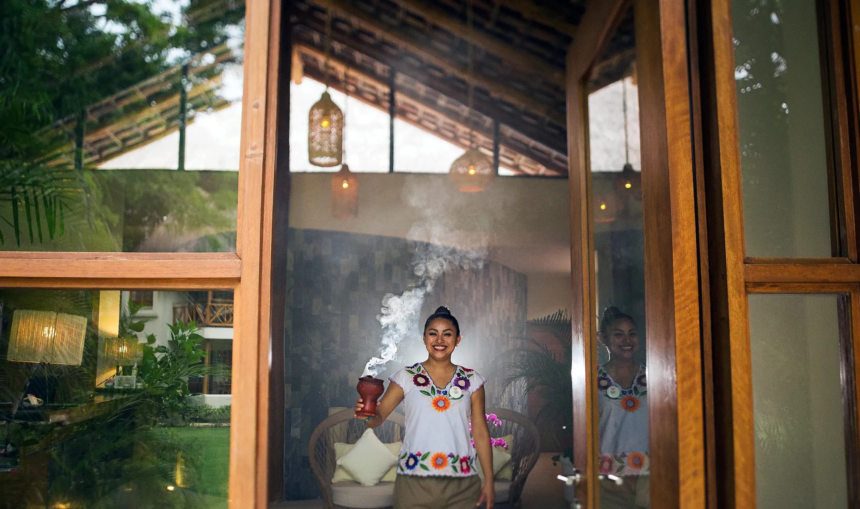 Staff member in traditional dress holding a smoking incense vessel at the spa entrance