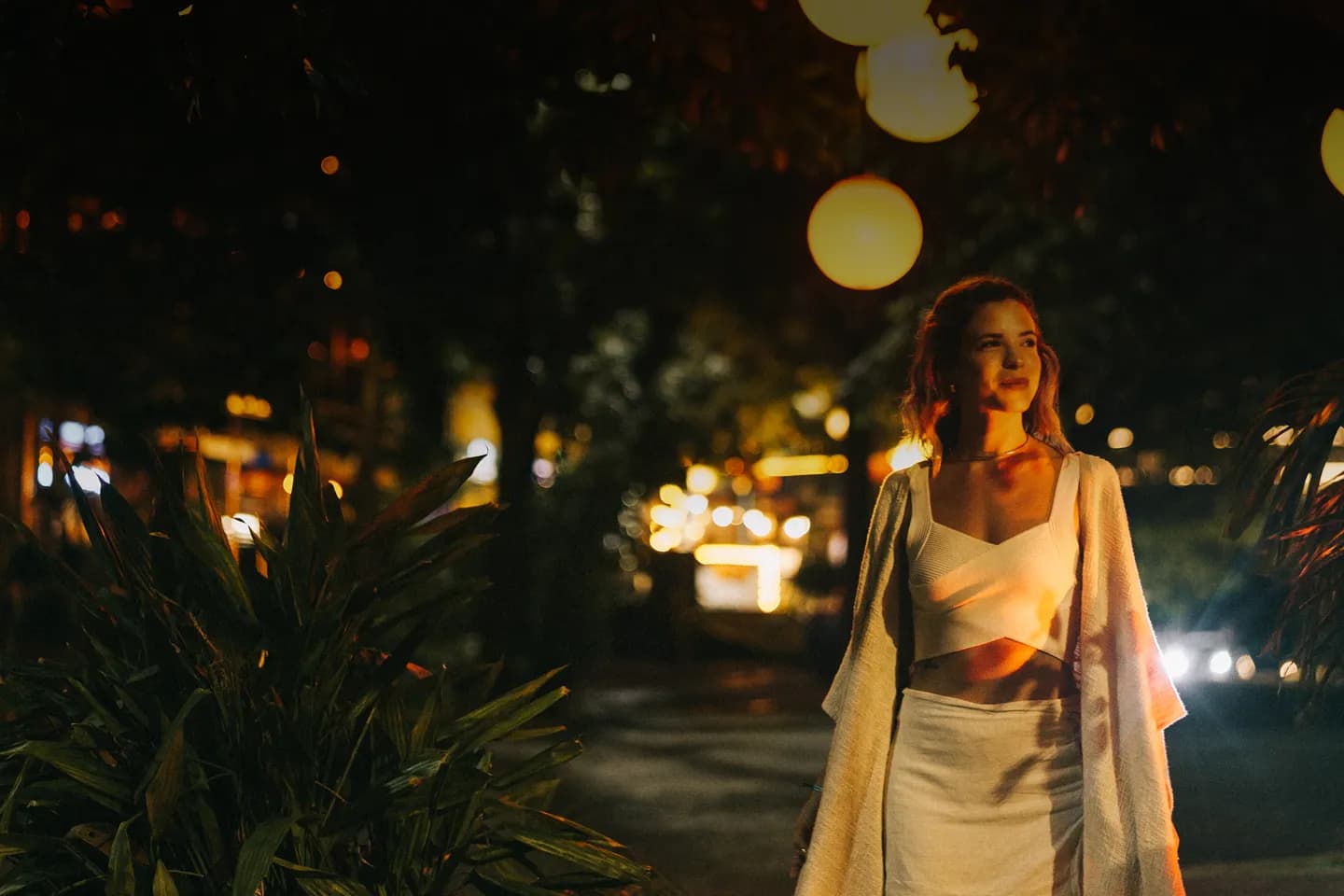 Woman walking at night among lights and palm trees on Fifth Avenue