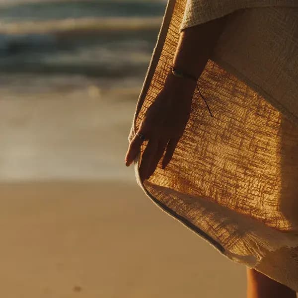 Close-up of a linen garment and a hand as someone walks along the beach at sunset